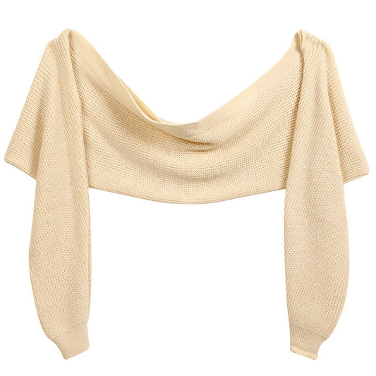 Beige knitted sleeved shawl displayed flat with a broad connecting panel, two long sleeves and ribbed-looking sleeve ends