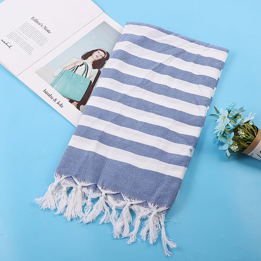 Blue and white striped Turkish towel folded on a blue surface with white twisted fringe
