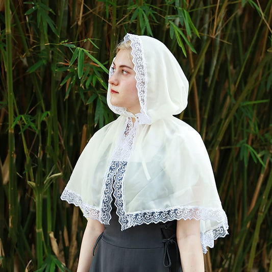 Model wearing a pale lace-trim hooded cape over a dark dress, with the front opening and shoulder drape visible