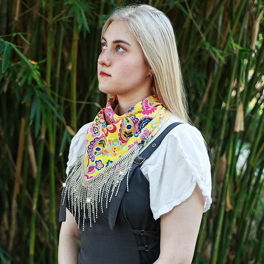 Yellow printed neck bandana with long reflective fringe worn over a white top and dark fitted outer layer