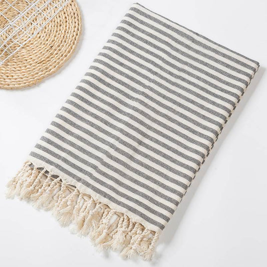 Folded grey and pale striped cotton towel with pale twisted fringe on a light surface